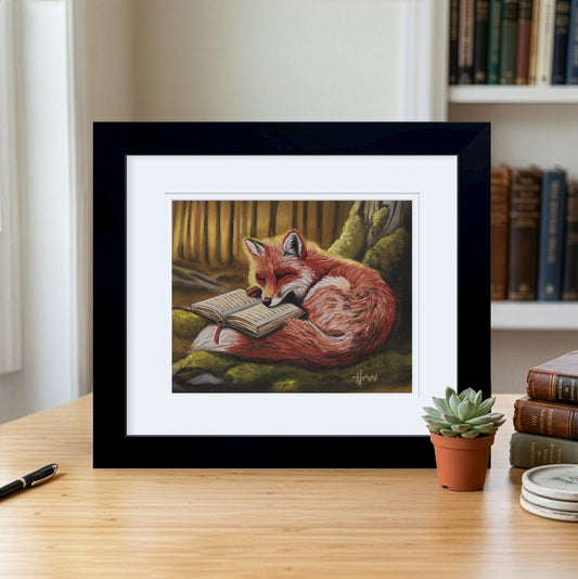 Framed artwork of a fox reading a book on a desk with books and a plant in the background.