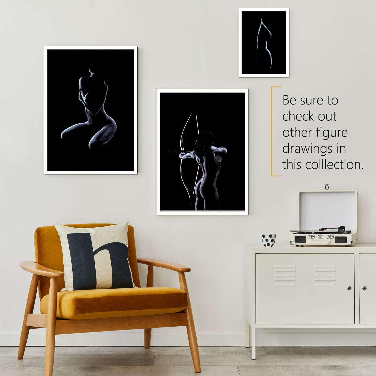 Three black and white pastel figure drawings hang on the wall in a seating area above an orange mid-century chair. A white locker cabinet sits to the right with a white retro vinyl record player on top. On the left sits a silver metal lamp.